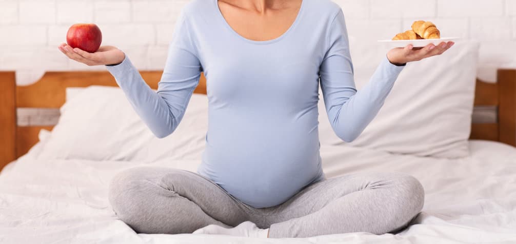 Unrecognizable Pregnant Woman Holding Apple And Croissants Sitting In Bed